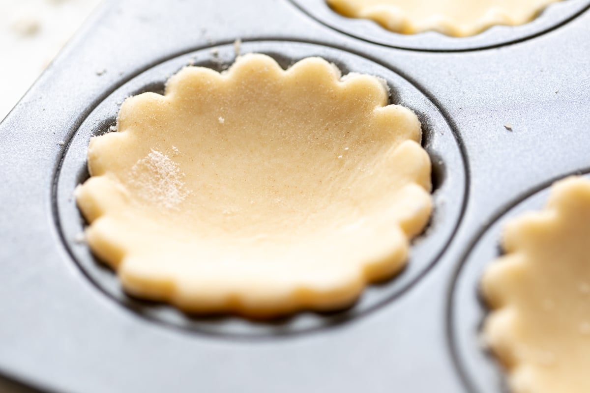 A mini tart crust inside a muffin tin, prior to baking.