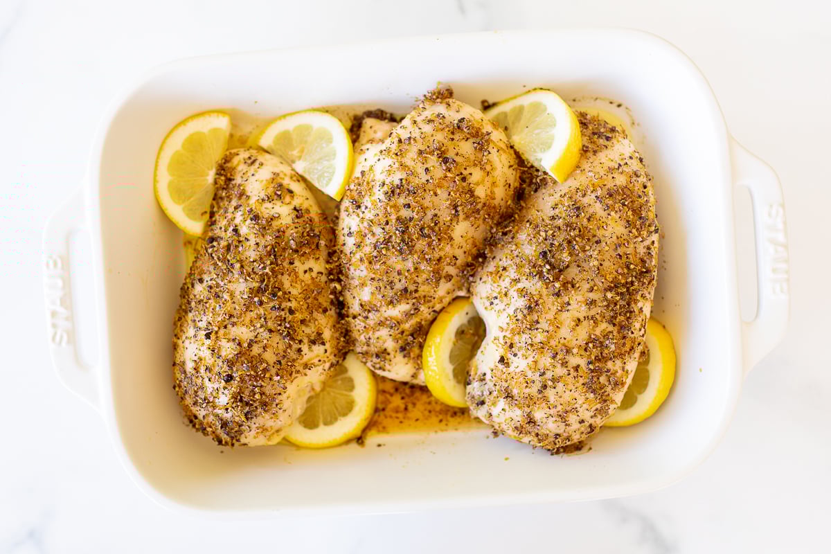 Baked lemon pepper chicken in a white baking dish.
