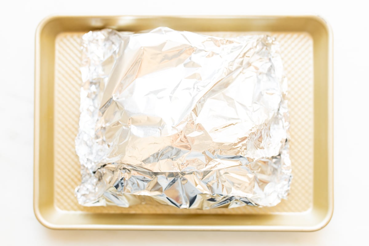 Foil wrapped salmon on a gold baking sheet.