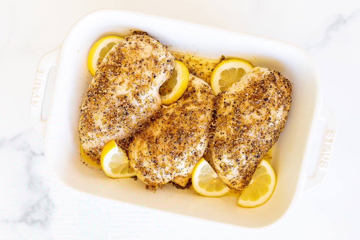 Baked lemon pepper chicken in a white baking dish.