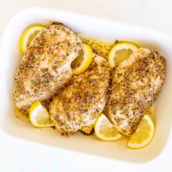 Baked lemon pepper chicken in a white baking dish.