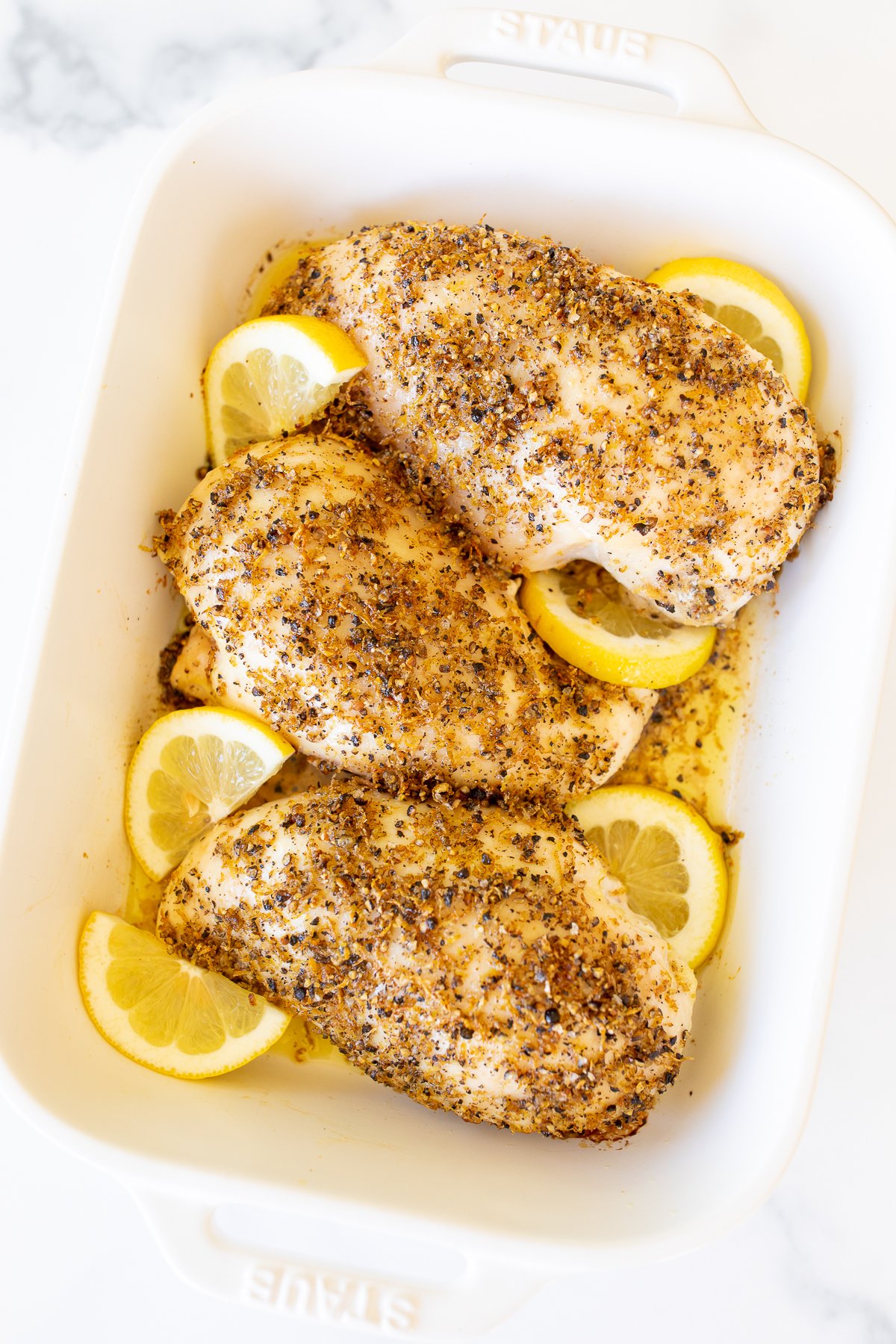 Baked lemon pepper chicken in a white baking dish. 