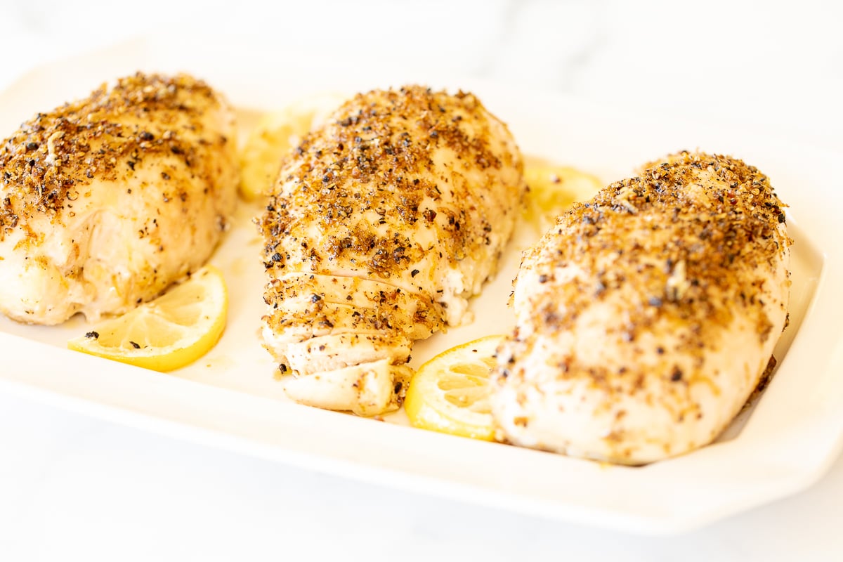 Baked lemon pepper chicken in a white baking dish.