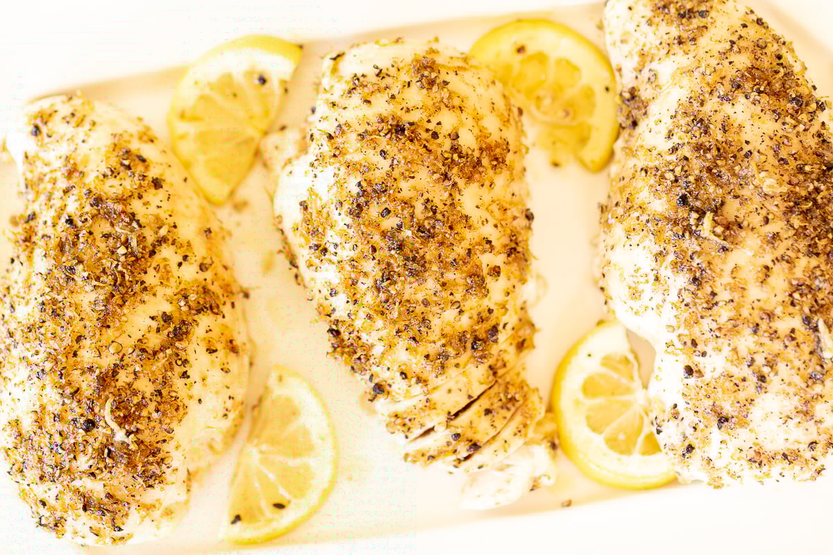 Baked lemon pepper chicken in a white baking dish.