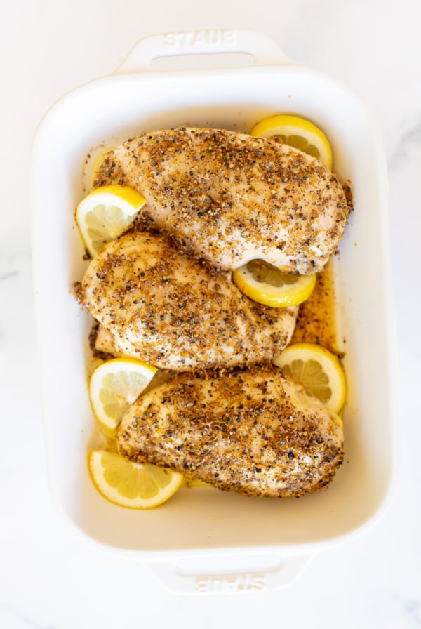 Baked lemon pepper chicken in a white baking dish.