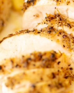 A sliced lemon pepper chicken breast on a white serving platter.