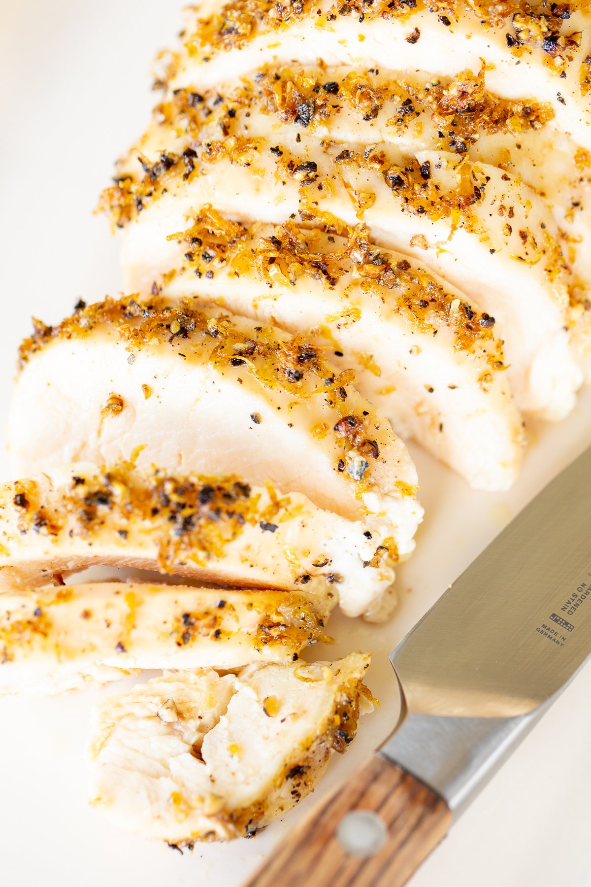 A sliced lemon pepper chicken breast on a white serving platter.