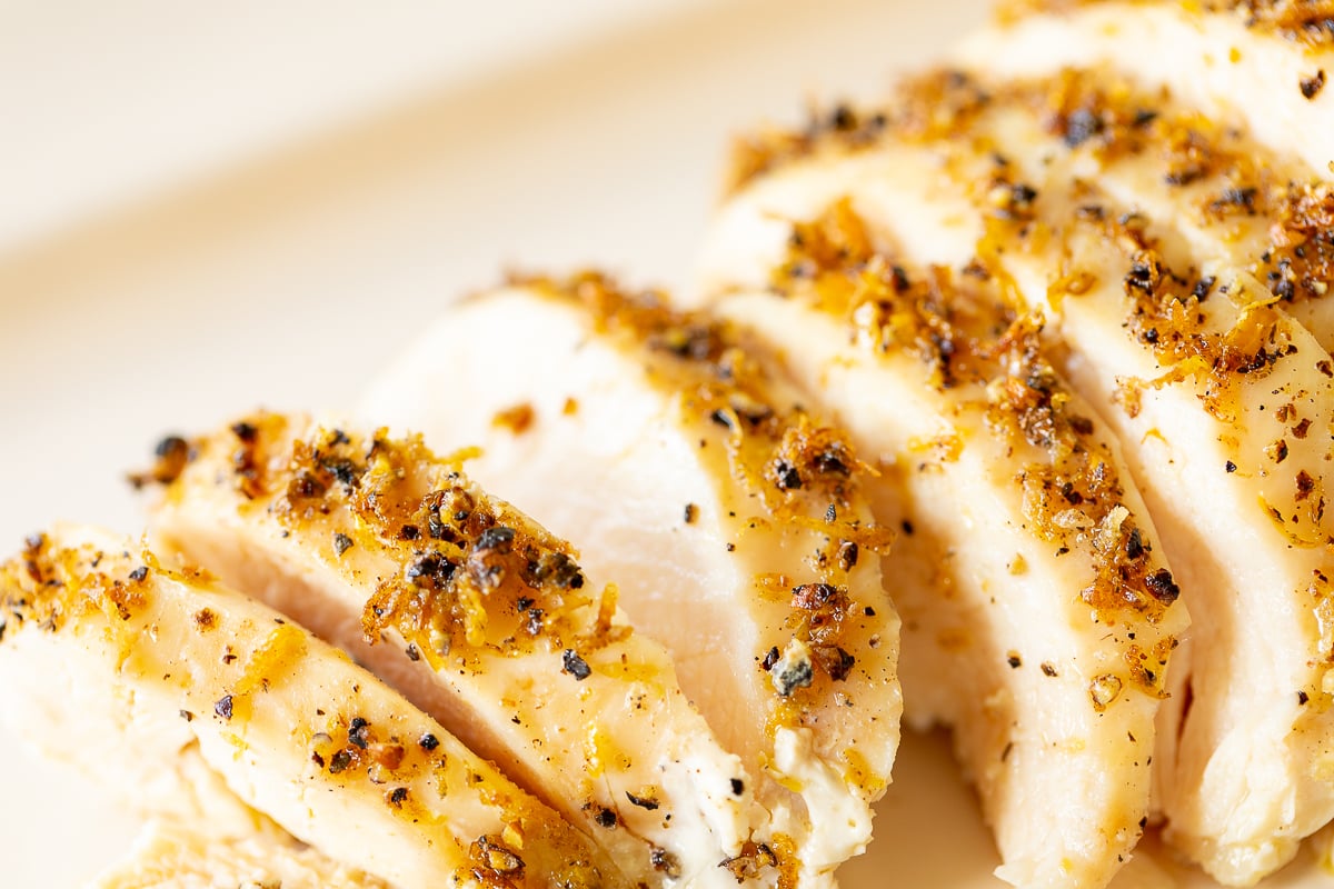 A sliced lemon pepper chicken breast on a white serving platter.