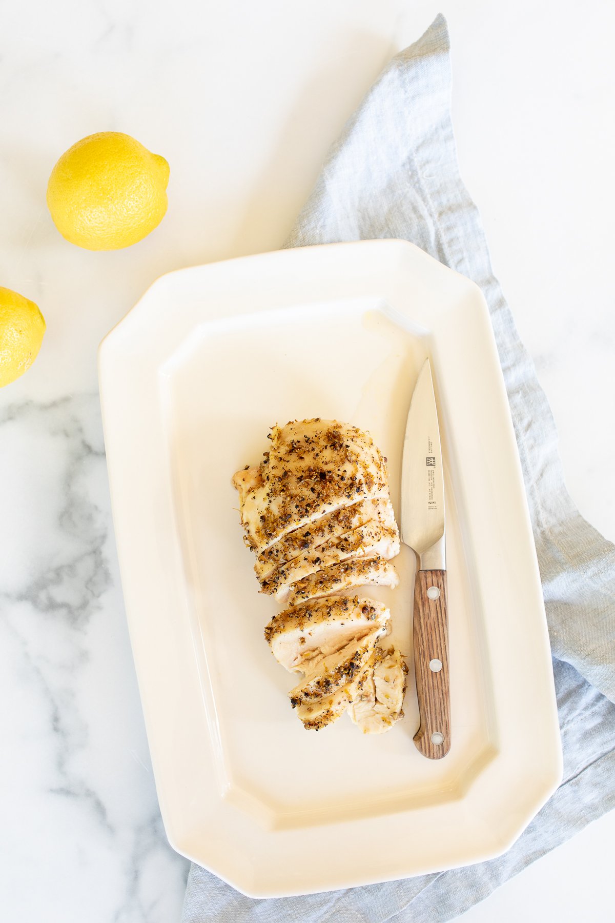 A sliced lemon pepper chicken breast on a white serving platter.