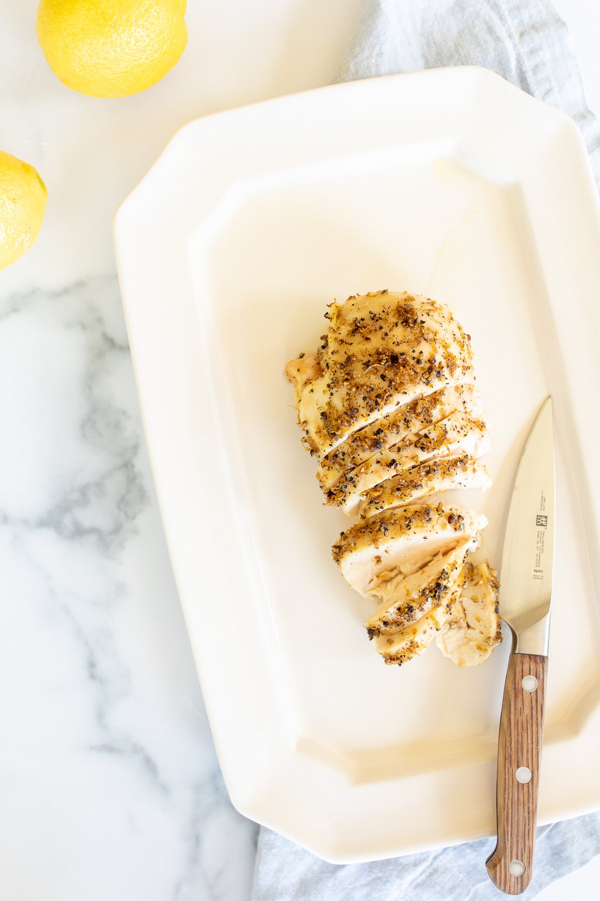 A sliced lemon pepper chicken breast on a white serving platter.