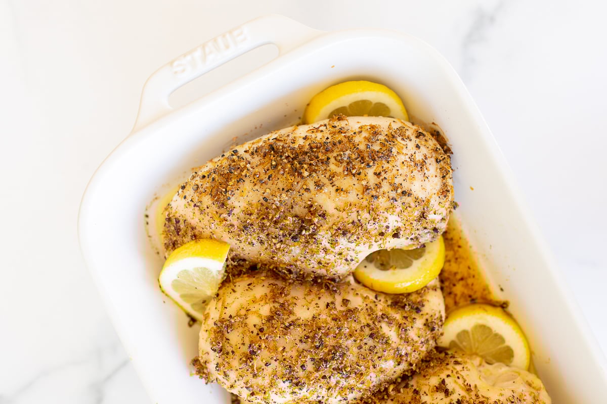 Baked lemon pepper chicken in a white baking dish.