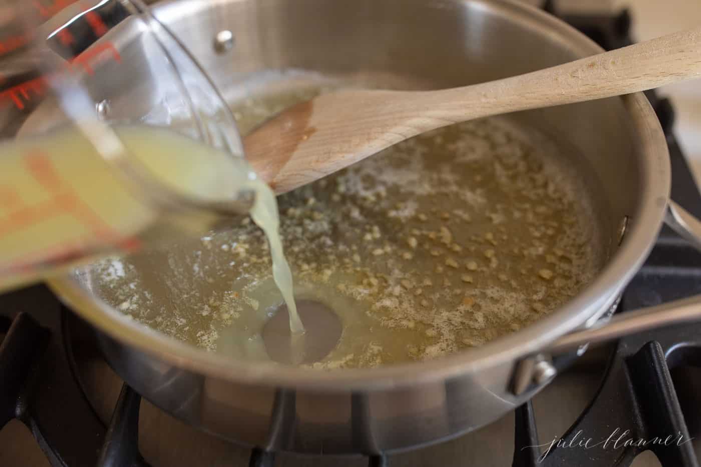 A silver pan on a stove top, melted butter and garlic being stirred with a wooden spatula.