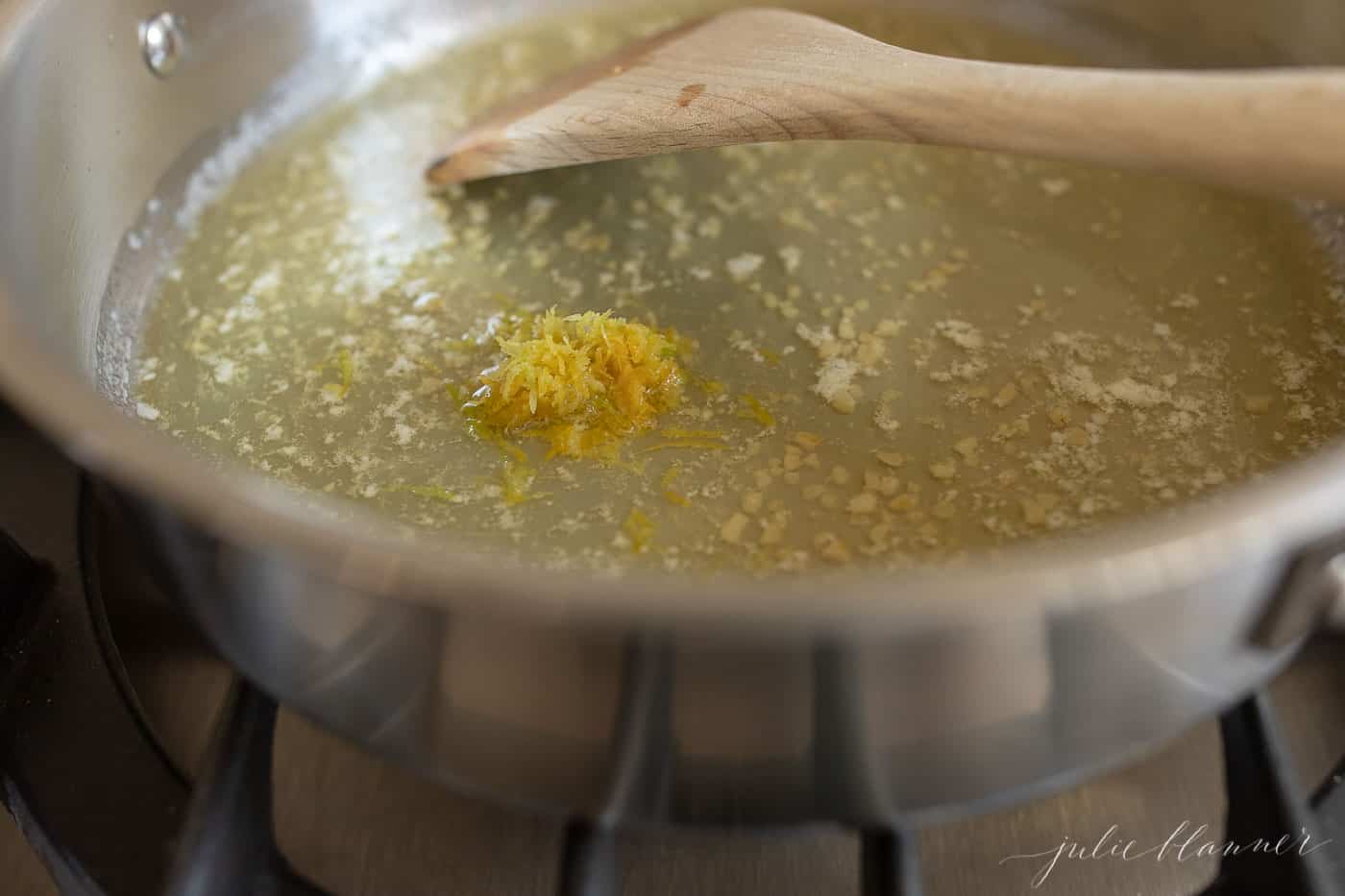 A silver pan on a stove top, melted butter and garlic being stirred with a wooden spatula.