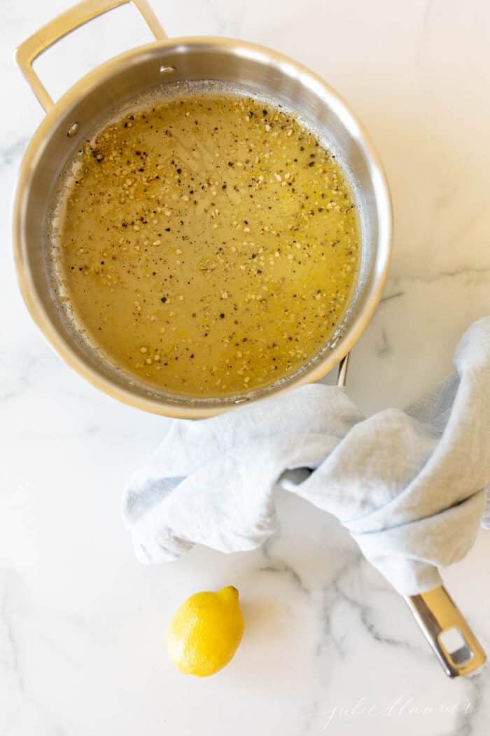 A saucepan on a marble surface, lemon pepper sauce inside.