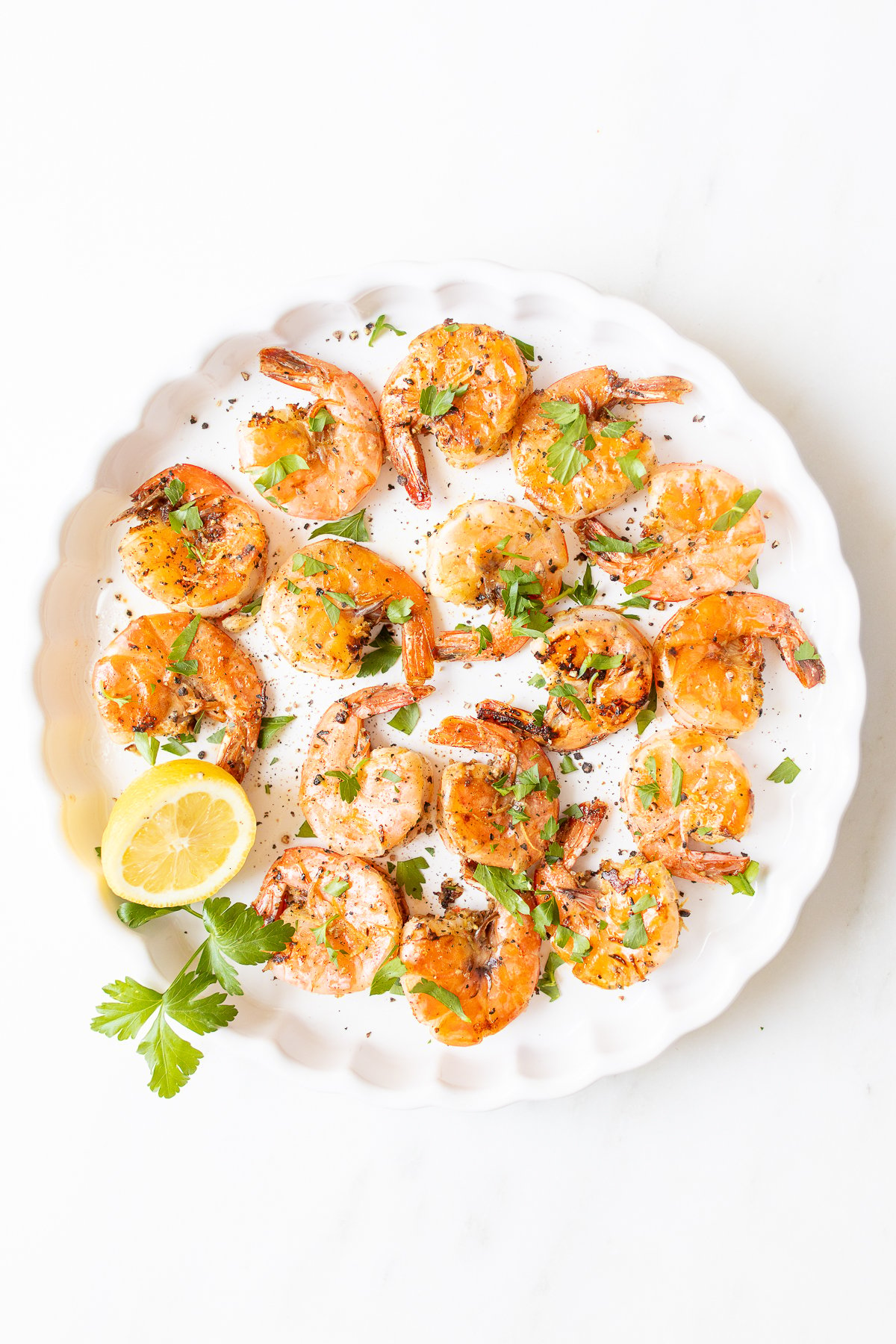 Lemon pepper shrimp on a round white serving platter.