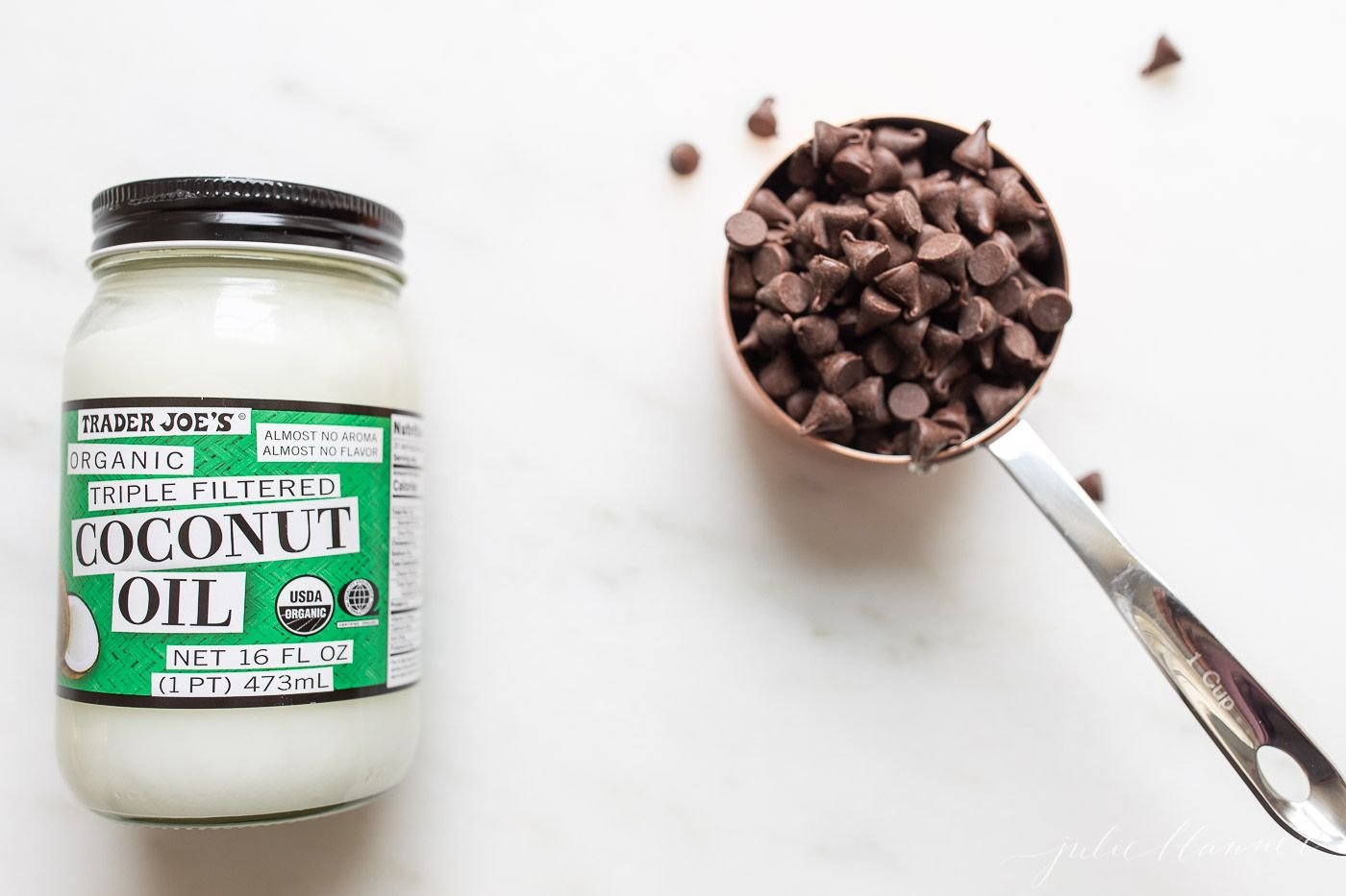 Chocolate chips and a jar of coconut oil on a marble countertop.