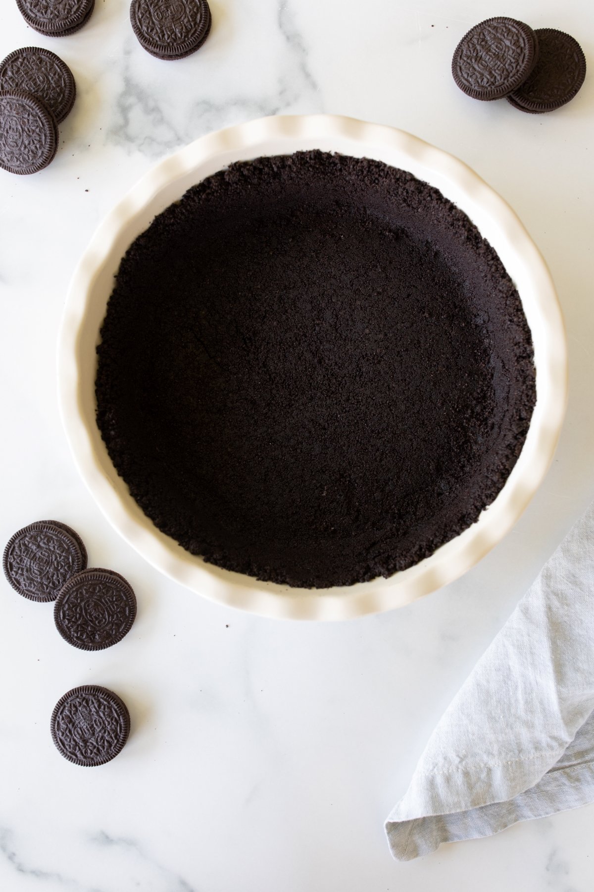 A white ceramic pie dish with an oreo crust recipe inside, oreos to the side.