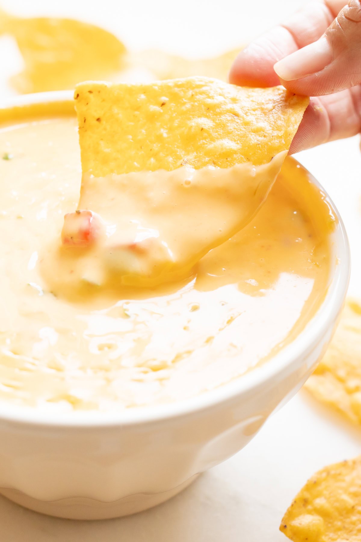 A hand dips a tortilla chip into a bowl of Velveeta cheese dip, laden with enticing, creamy chunks.