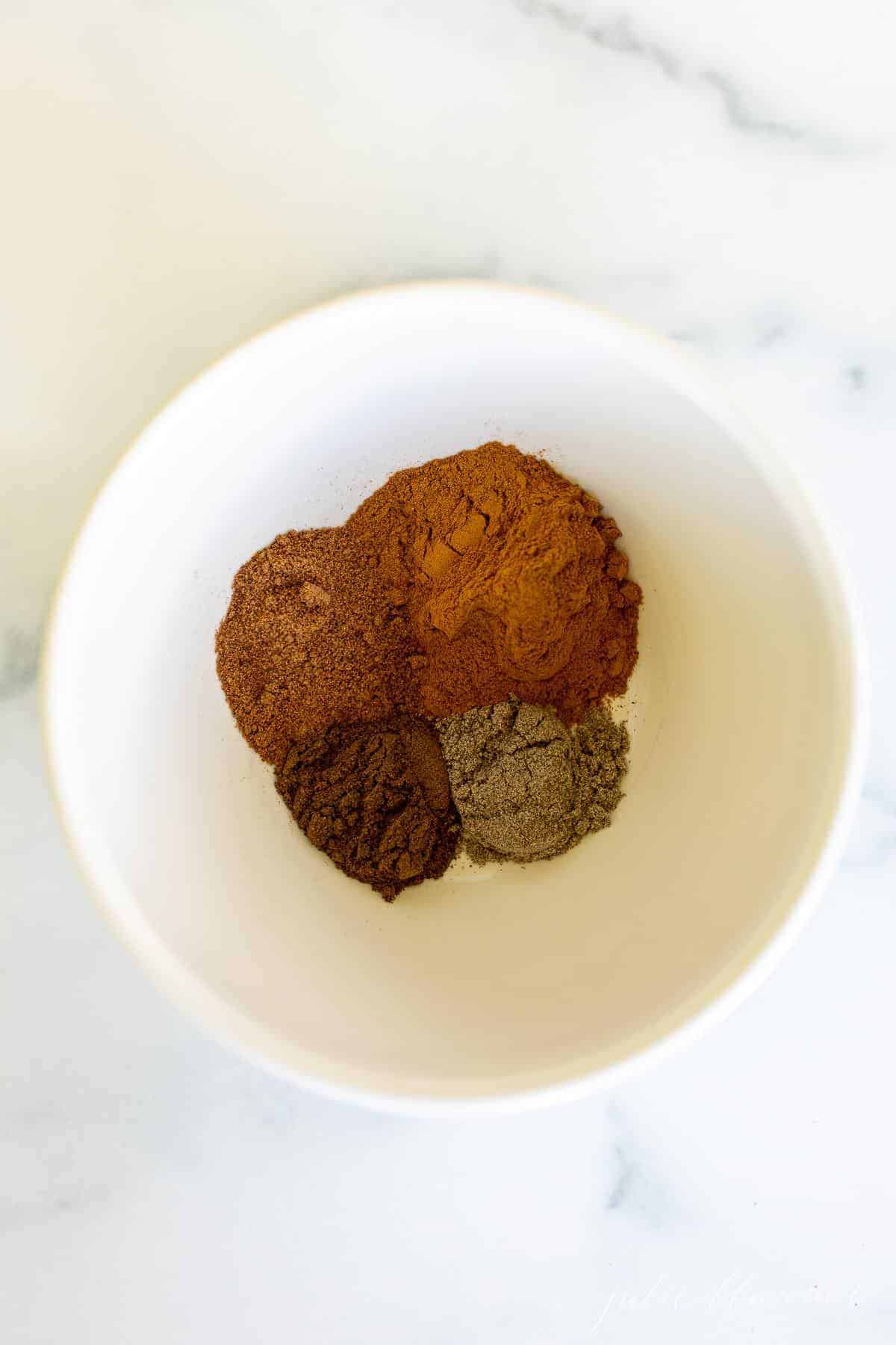 A white bowl full of seasonings to make an apple pie spice recipe.