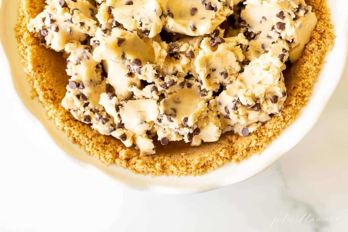 Cookie dough pie filling inside a homemade pie crust on a marble surface.