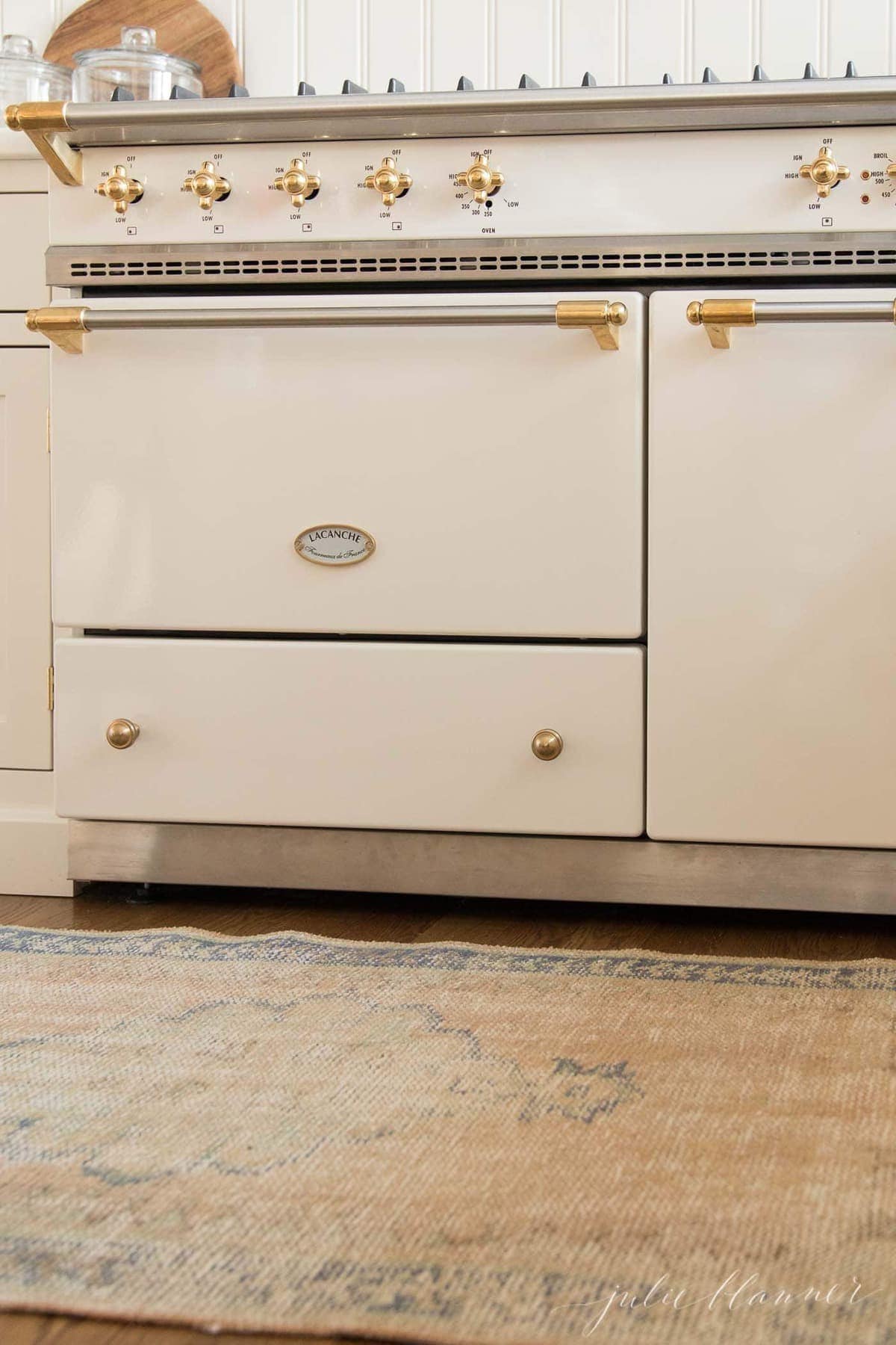 A rug on a wood floor in front of a cream French range in a kitchen.