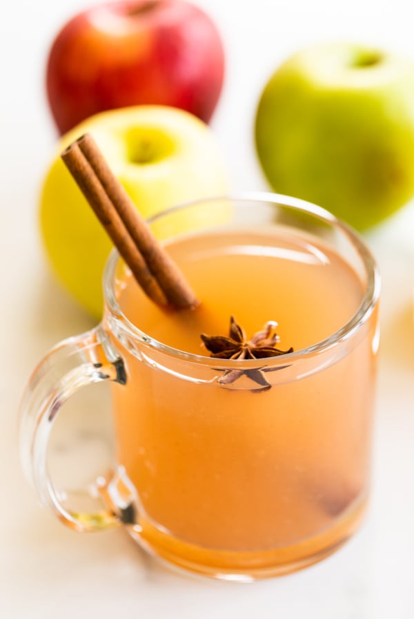 A clear glass mug full of homemade apple cider, with apples in the background.