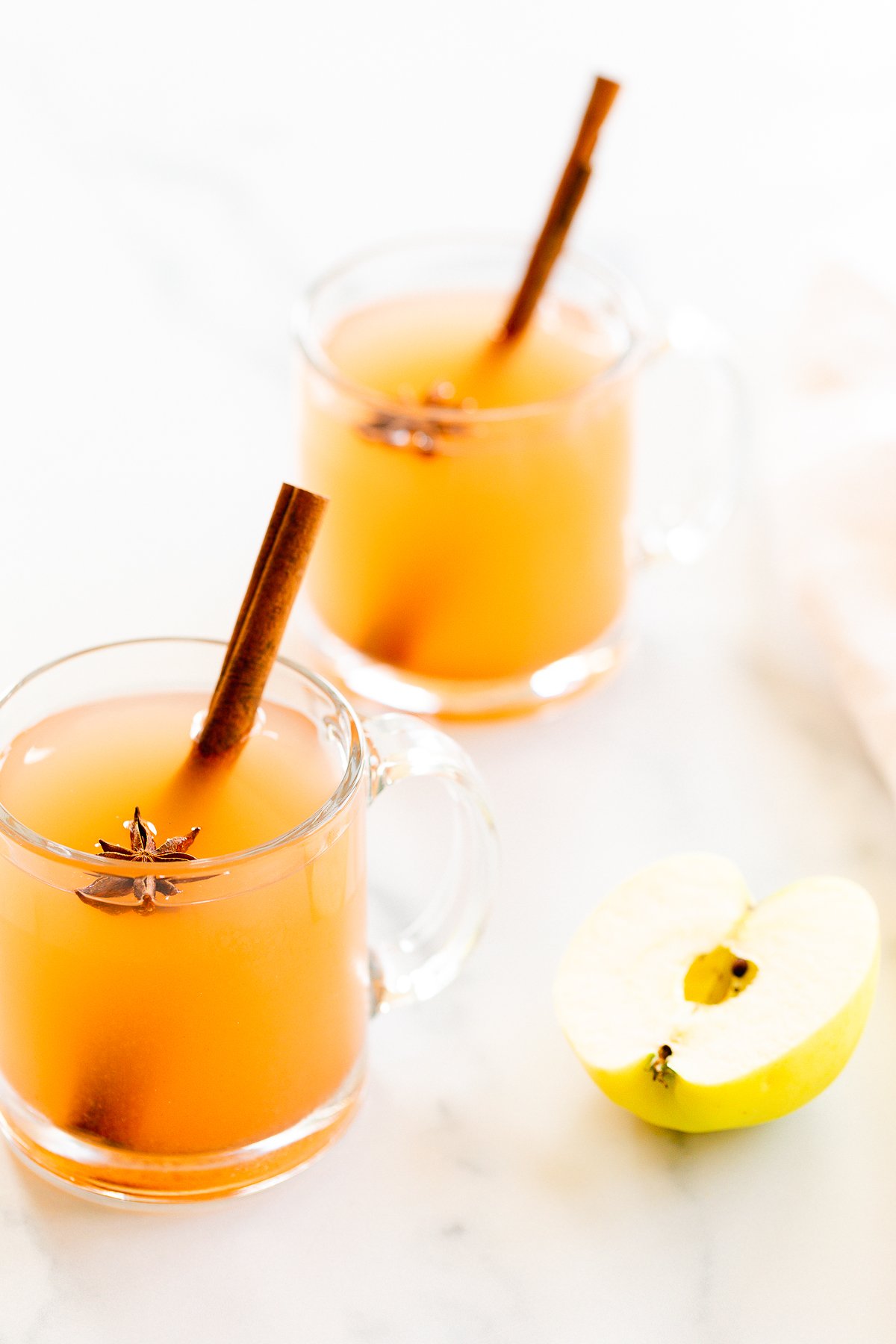 A clear glass mug full of homemade apple cider, with apples in the background.