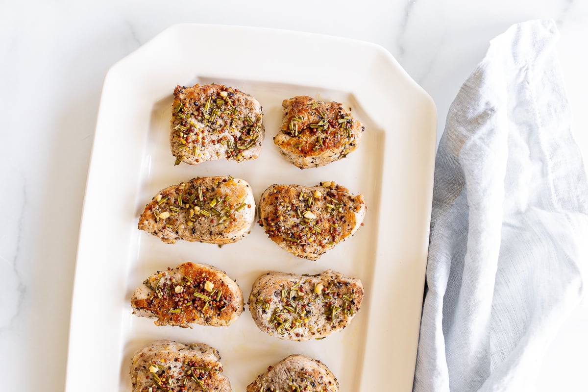 Apple cider pork tenderloin medallions on a white platter.