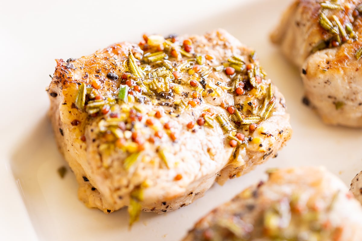 Apple cider pork tenderloin medallions on a white platter.