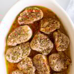 Apple cider pork tenderloin medallions in a white baking dish.