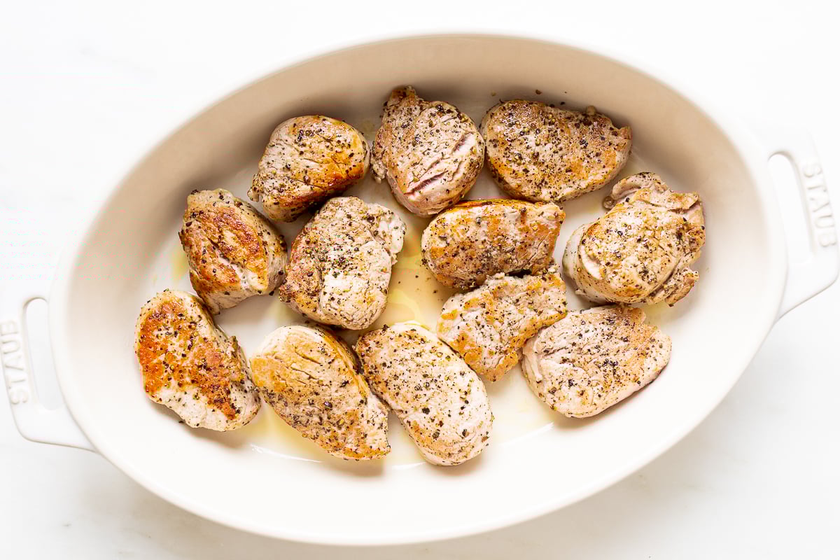 Apple cider pork tenderloin medallions in a white baking dish.