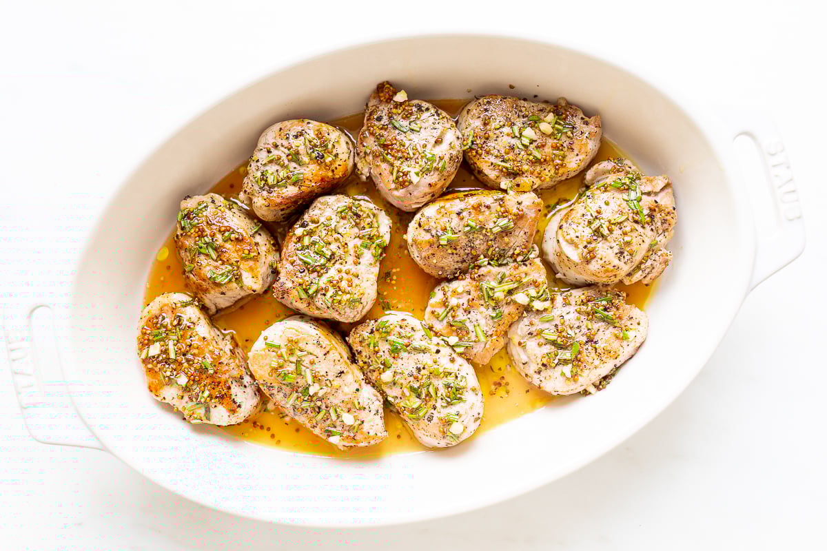 Apple cider pork tenderloin medallions in a white baking dish.