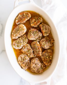 Apple cider pork tenderloin medallions in a white baking dish.