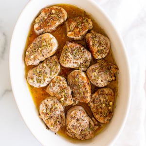 Apple cider pork tenderloin medallions in a white baking dish.