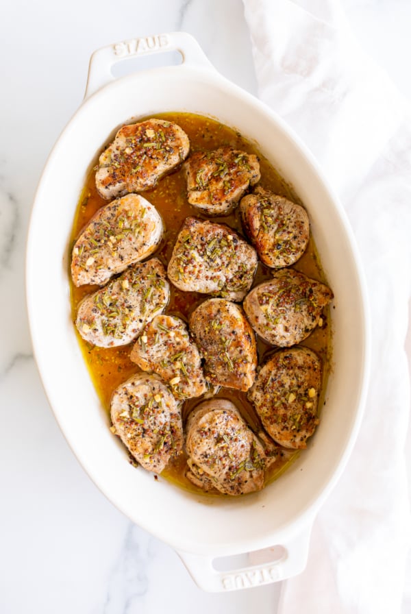 Apple cider pork tenderloin medallions in a white baking dish.