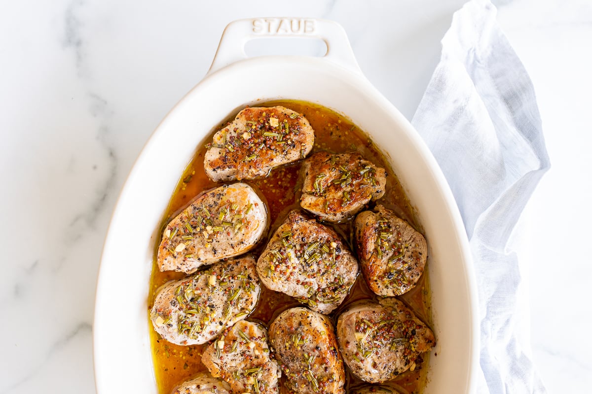 Apple cider pork tenderloin medallions in a white baking dish.