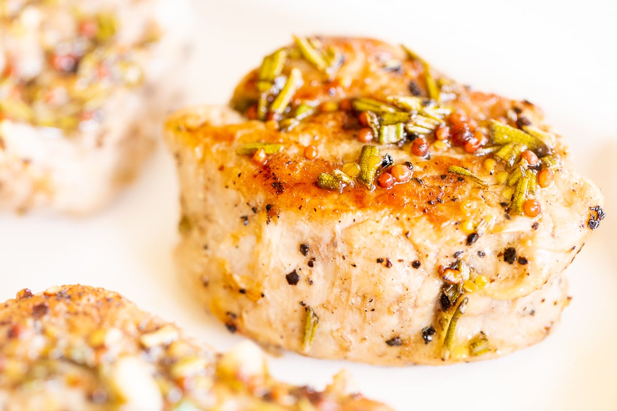 Apple cider pork tenderloin medallions on a white platter.