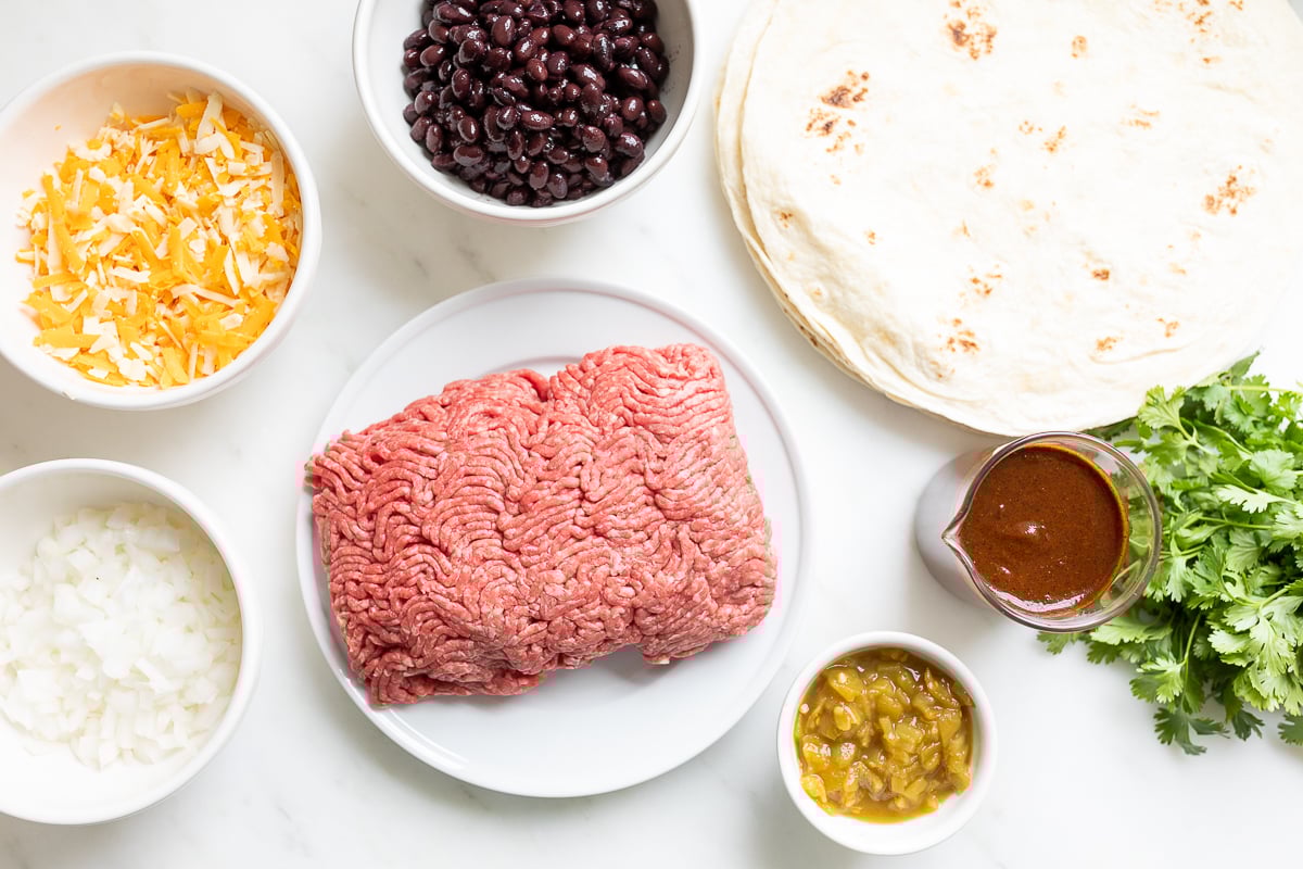 ingredients for beef enchiladas spread out on a white countertop.