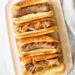 A white tray filled with bratwurst sausages in buns.