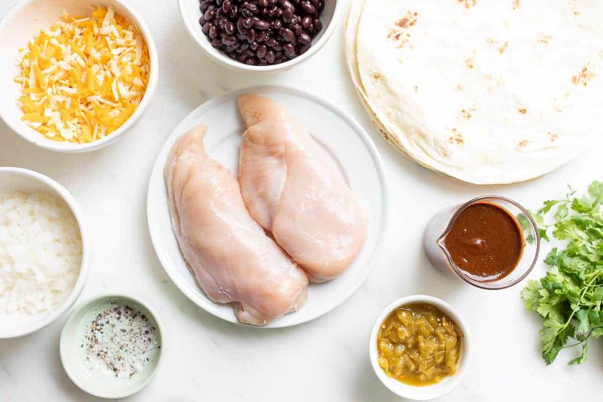 The ingredients for a chicken enchilada recipe on a marble surface.