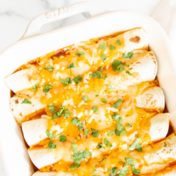 A white baking dish full of chicken enchiladas.