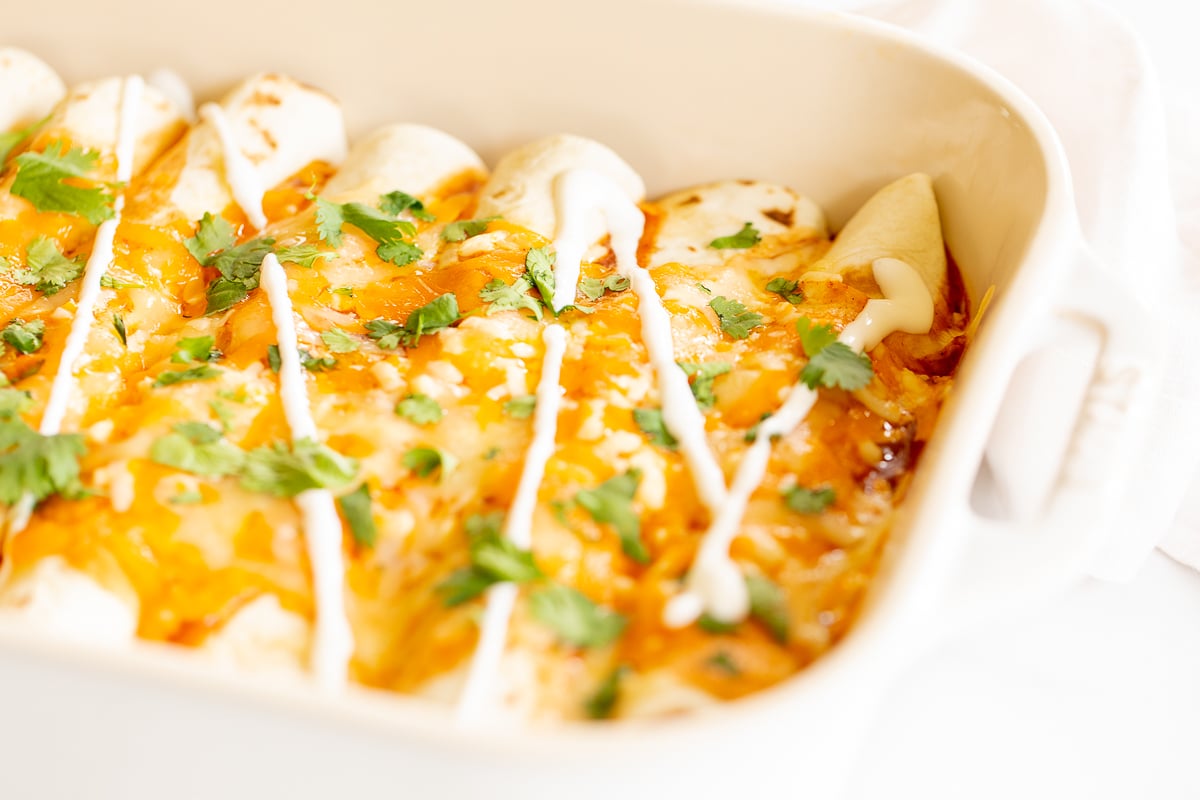 A white baking dish full of chicken enchiladas.