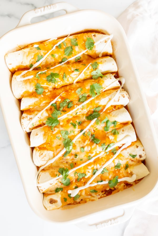 A white baking dish full of chicken enchiladas.