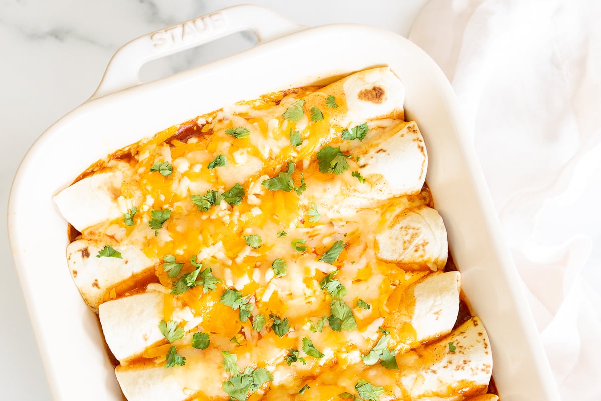 A white baking dish full of chicken enchiladas.