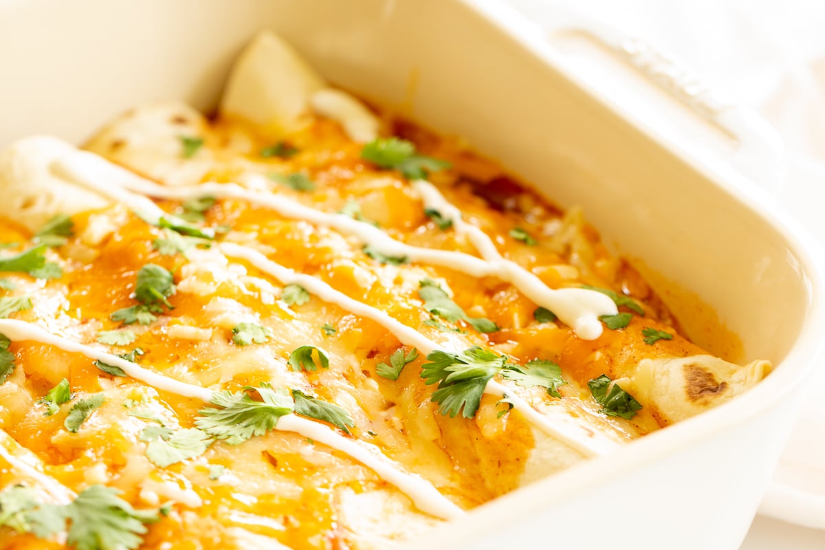 A white baking dish full of chicken enchiladas.