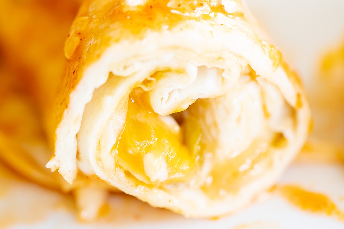 A close up shot of a cut open enchilada in a chicken enchilada recipe.