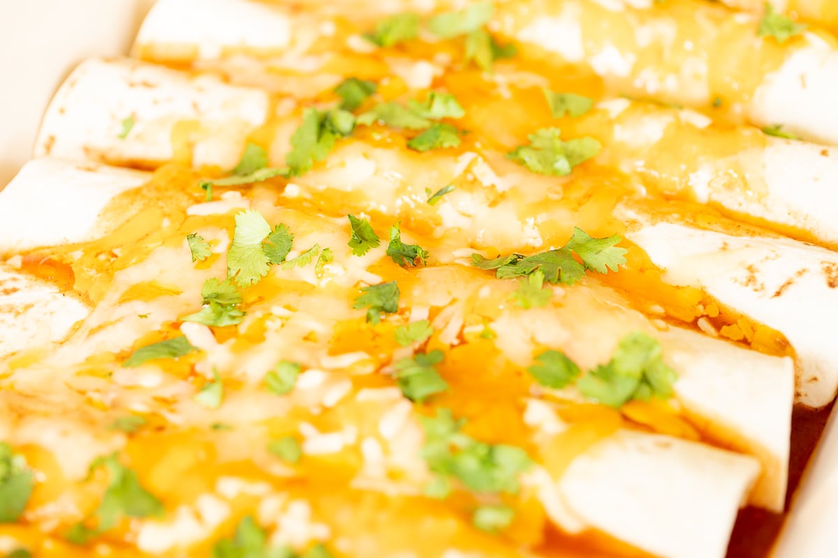 A white baking dish full of chicken enchiladas.