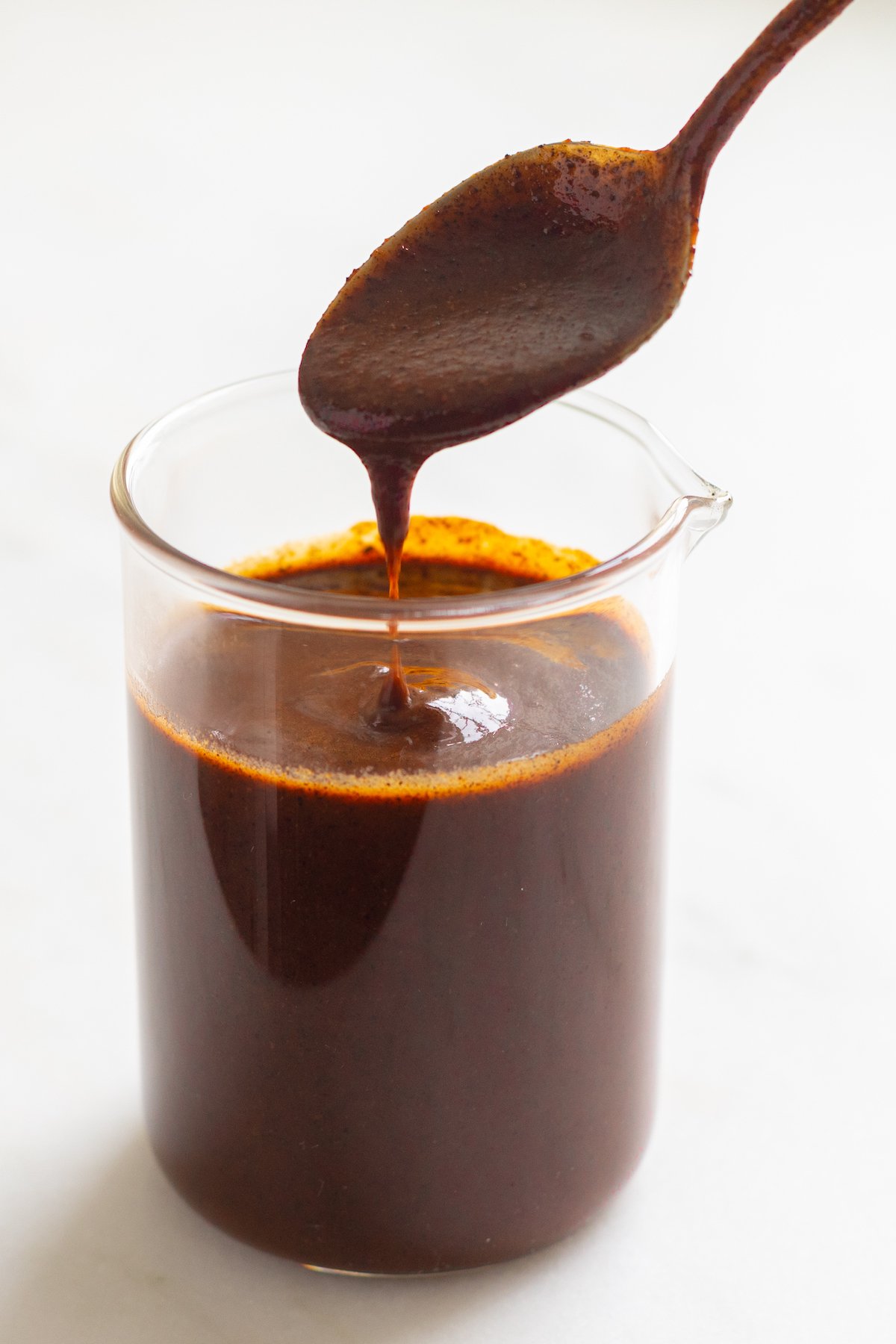 A small clear glass jar filled with enchilada sauce on a white countertop.