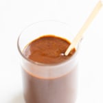 A small clear glass jar filled with enchilada sauce on a white countertop.