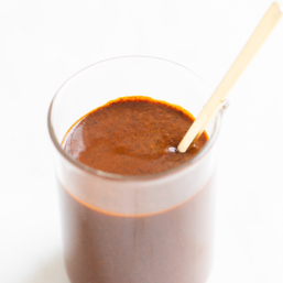 A small clear glass jar filled with enchilada sauce on a white countertop.